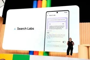 A speaker on stage presents Search Labs. Behind them is a large screen displaying a phone interface with a search query about seeing a shooting star. The screen shows information and graphics related to Search Labs, with colorful vertical pillars in the background, reminiscent of Netflix's vibrant interface. CodersLink 2024.