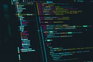 Close-up of a computer screen displaying a code editor with a dark theme. The screen shows several open files in a sidebar on the left, with colorful syntax-highlighted code for proyectos using React in JavaScript on the main workspace to the right. CodersLink 2024.