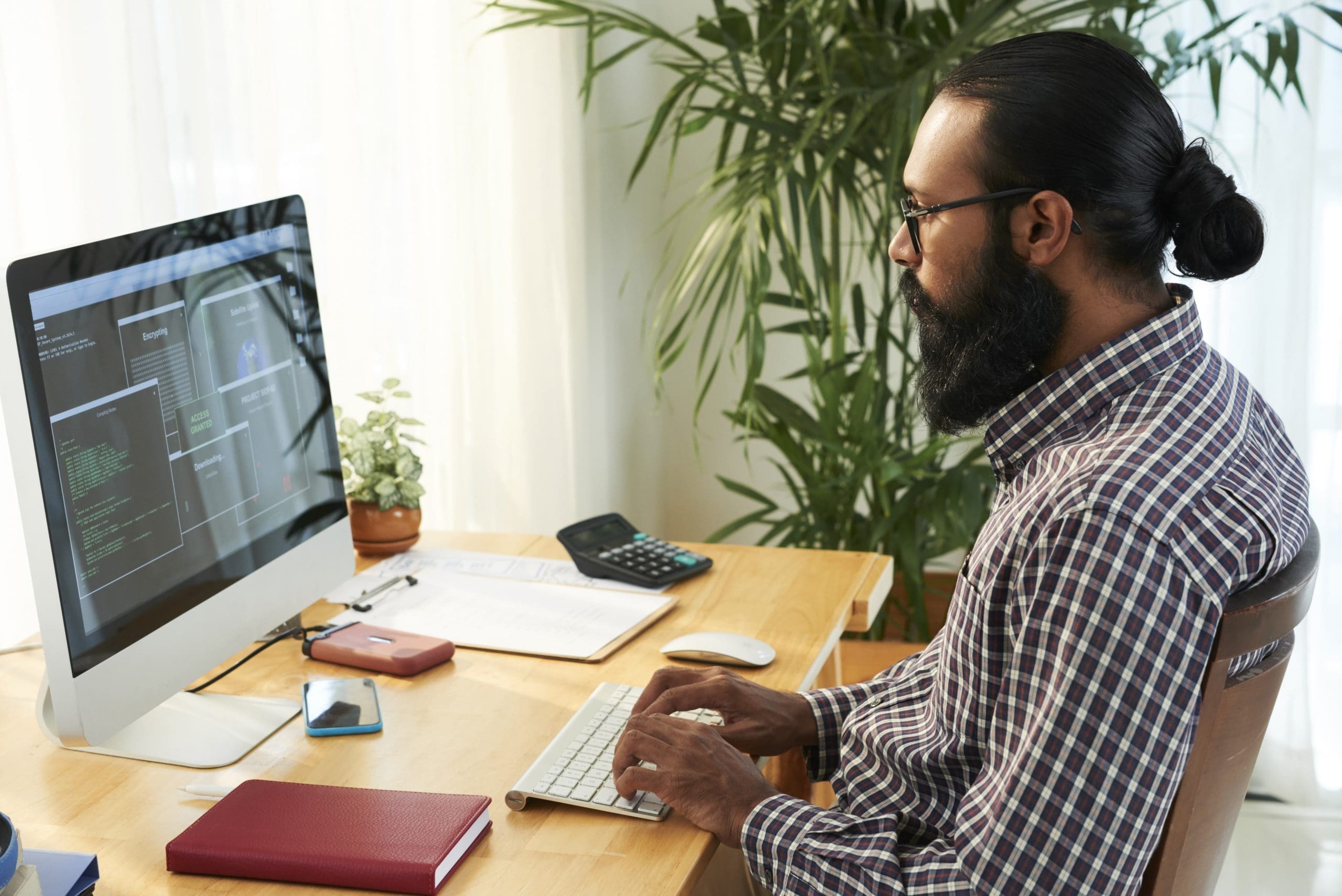 Programador móvil en ropa informal sentado junto al escritorio frente al monitor de la computadora mientras desarrolla una nueva app